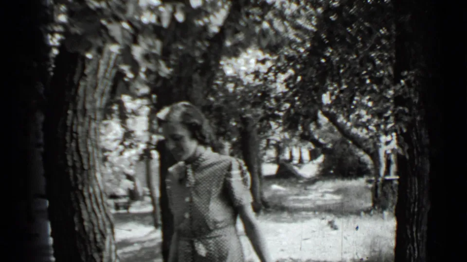 Adult woman passes close to the camera beside a large tree trunk in 1939 Clear Lake home-movie footage.