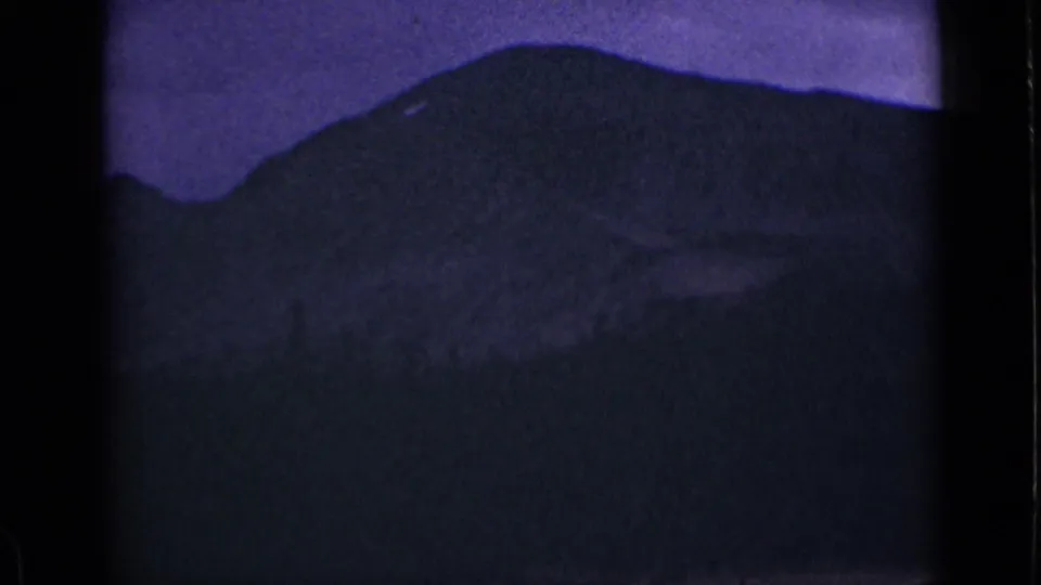 1939 Colorado home-movie frame with a dark rounded mountain, faint foreground detail, purple twilight, and visible 8mm texture.