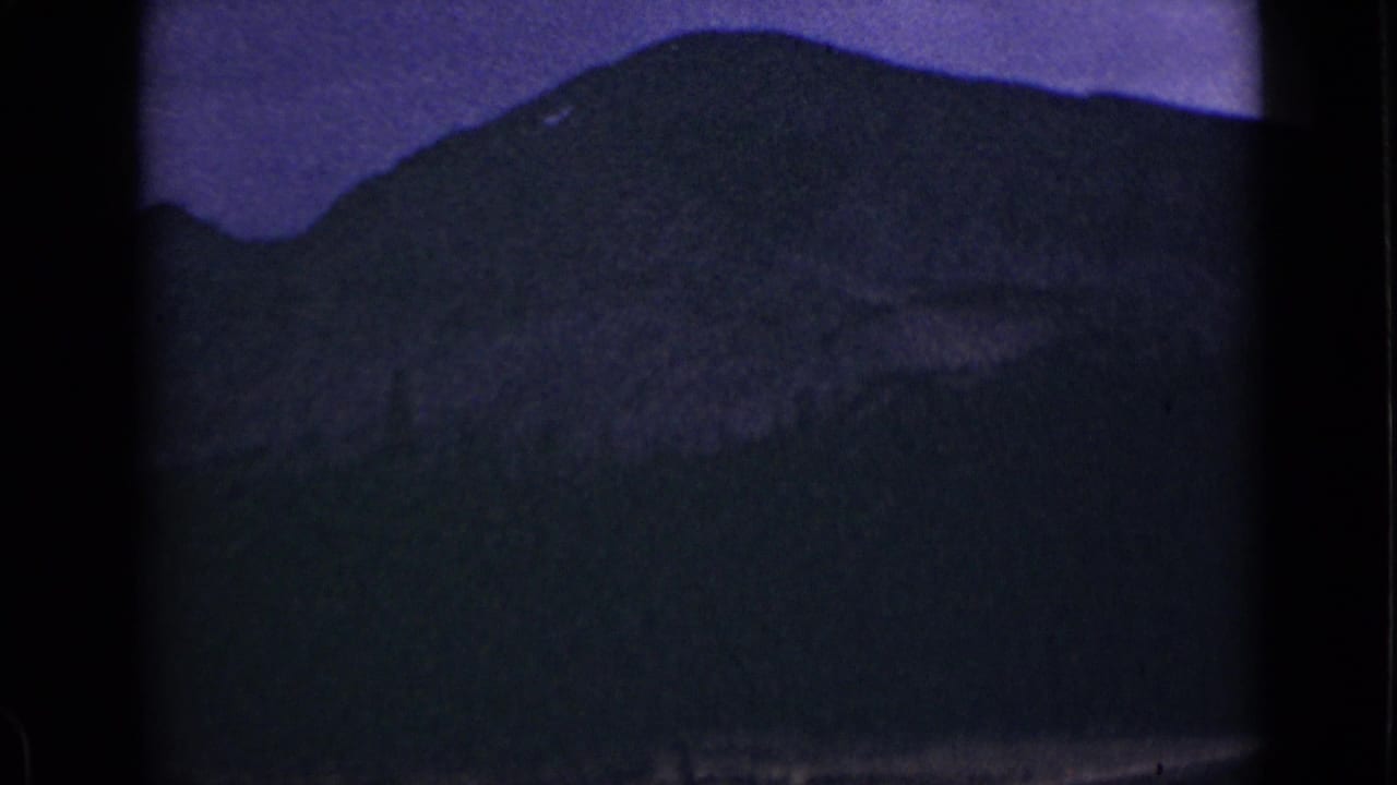 Dark 8mm frame showing a mountain lake and silhouetted ridge under a purple cast.