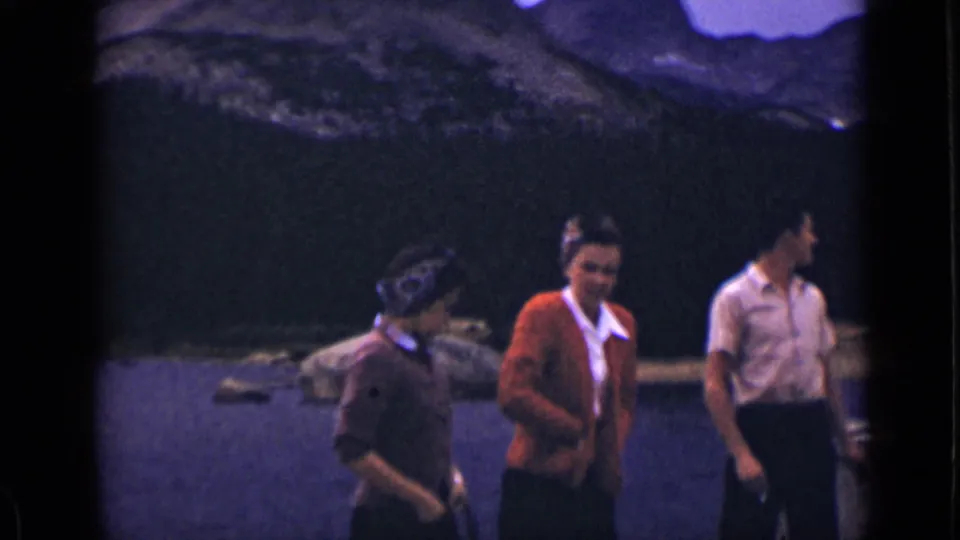 Three adults stand on a wooden dock at a Colorado mountain lake in 1939, with peaks and water behind them.