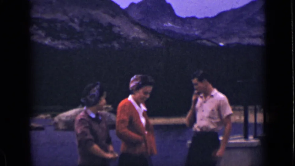 Three adults appear to converse on a wooden dock at a 1939 Colorado mountain lake, framed by dark 8mm borders.