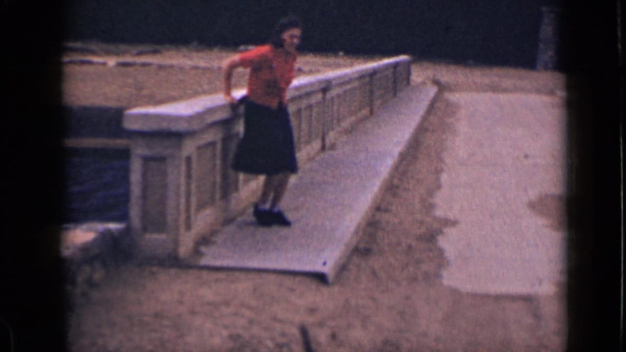 Woman in a red shirt steps from a low concrete railing beside a ramp.