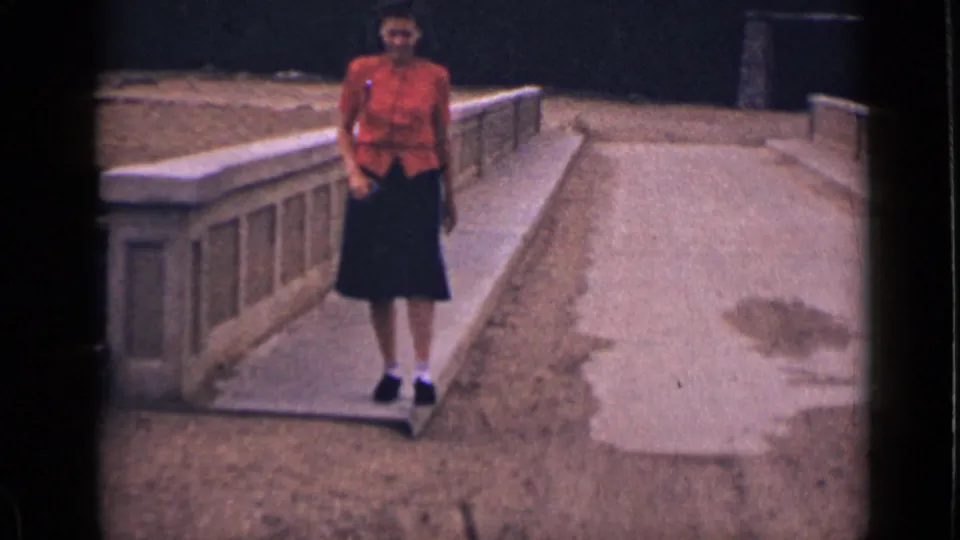 The woman faces the camera on a concrete walkway in Colorado, wearing a red shirt, dark skirt, white socks, and black shoes.