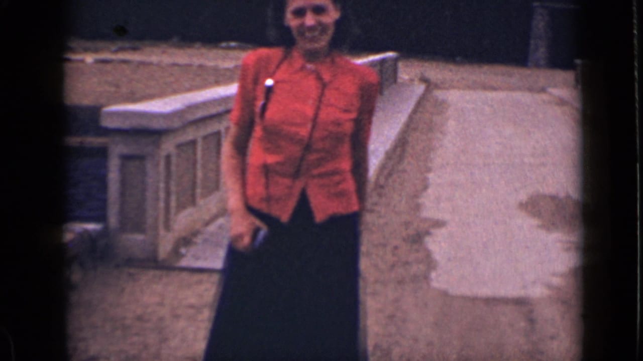 Woman in a red blouse and dark skirt walking on a paved path.