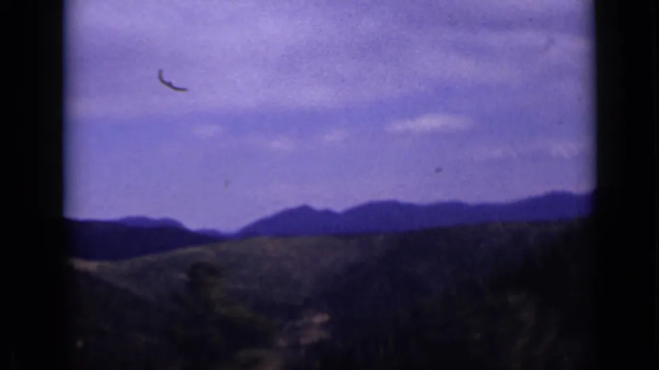 Colorado mountain scenery with layered ridges, dark foreground brush, and a cloudy sky in vintage 8mm color footage.