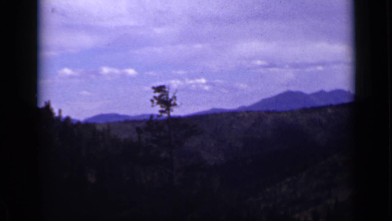 Distant mountain ridge beyond a dark forested valley, framed by black edges.