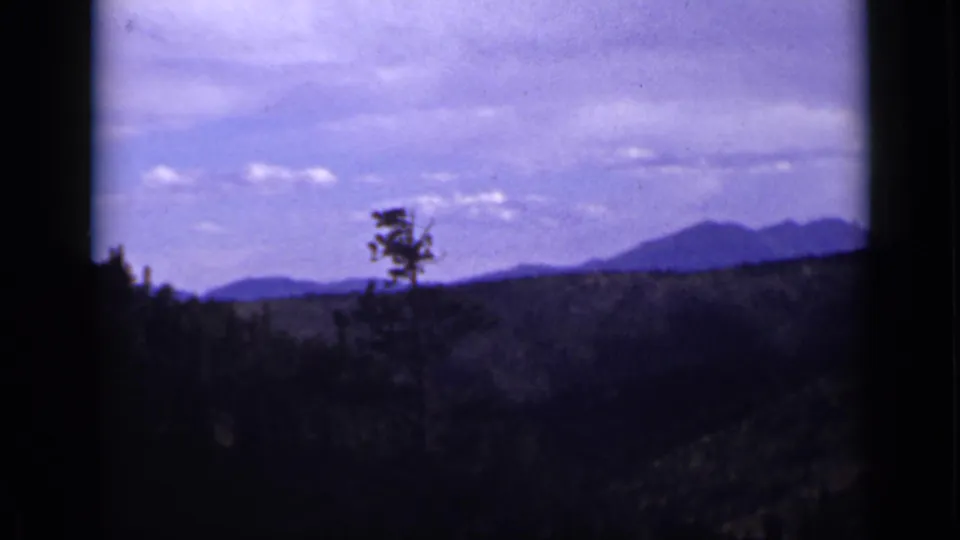 1939 Colorado 8mm frame showing a pine-dotted valley and distant mountain horizon beneath a pale, clouded sky.