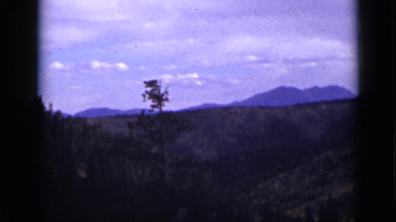 Forested valley and distant mountains seen through a dark vertical frame.
