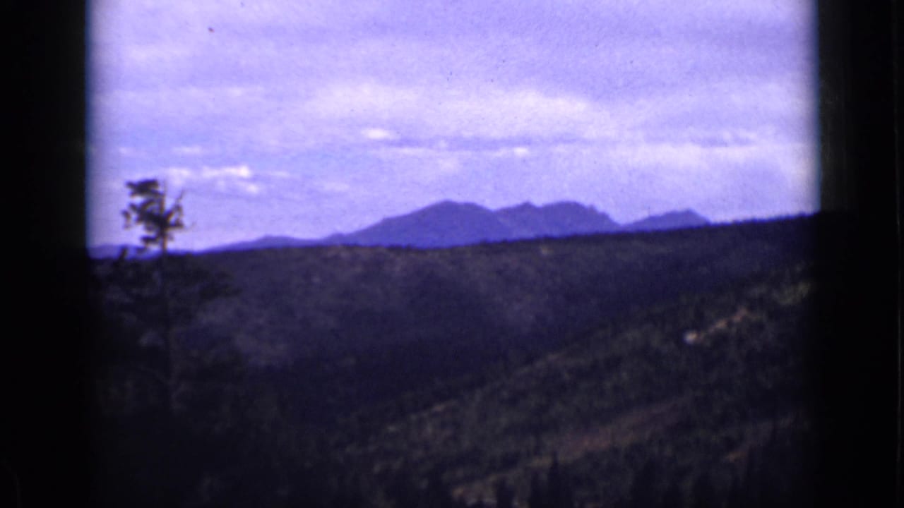 Forested hills and distant mountains under a pale clouded sky, framed by dark film edges.