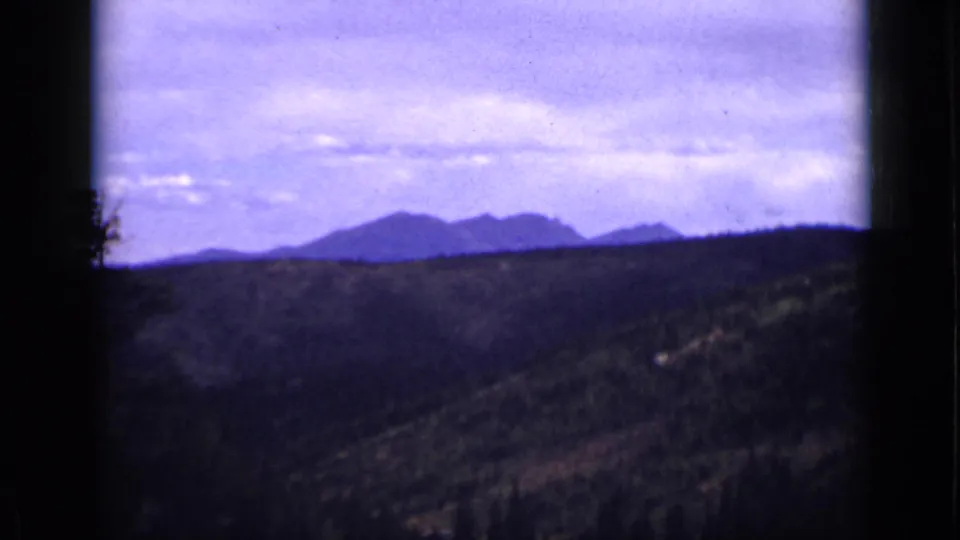 1939 Colorado 8mm view of dark wooded hills leading toward a soft distant mountain ridge below low clouds.