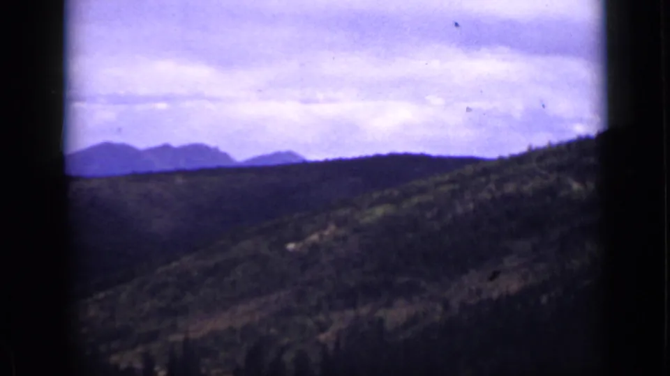 1939 Colorado 8mm view of forested slopes descending toward distant mountains under a pale, cloud-heavy sky.