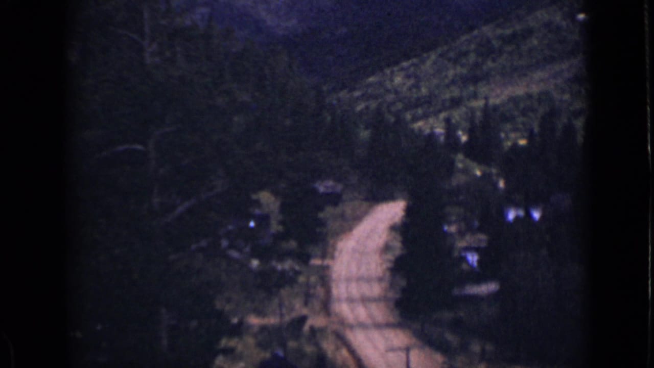 Pale dirt road curves through dark wooded hills with film gate edges visible.