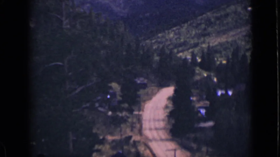 Soft 1939 Colorado 8mm frame of a pale rural road passing through dense woods toward hills.