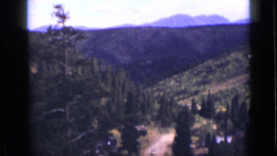 1939 Colorado 8mm frame showing a mountain ridge beyond pine forest and a winding dirt road in the valley below.