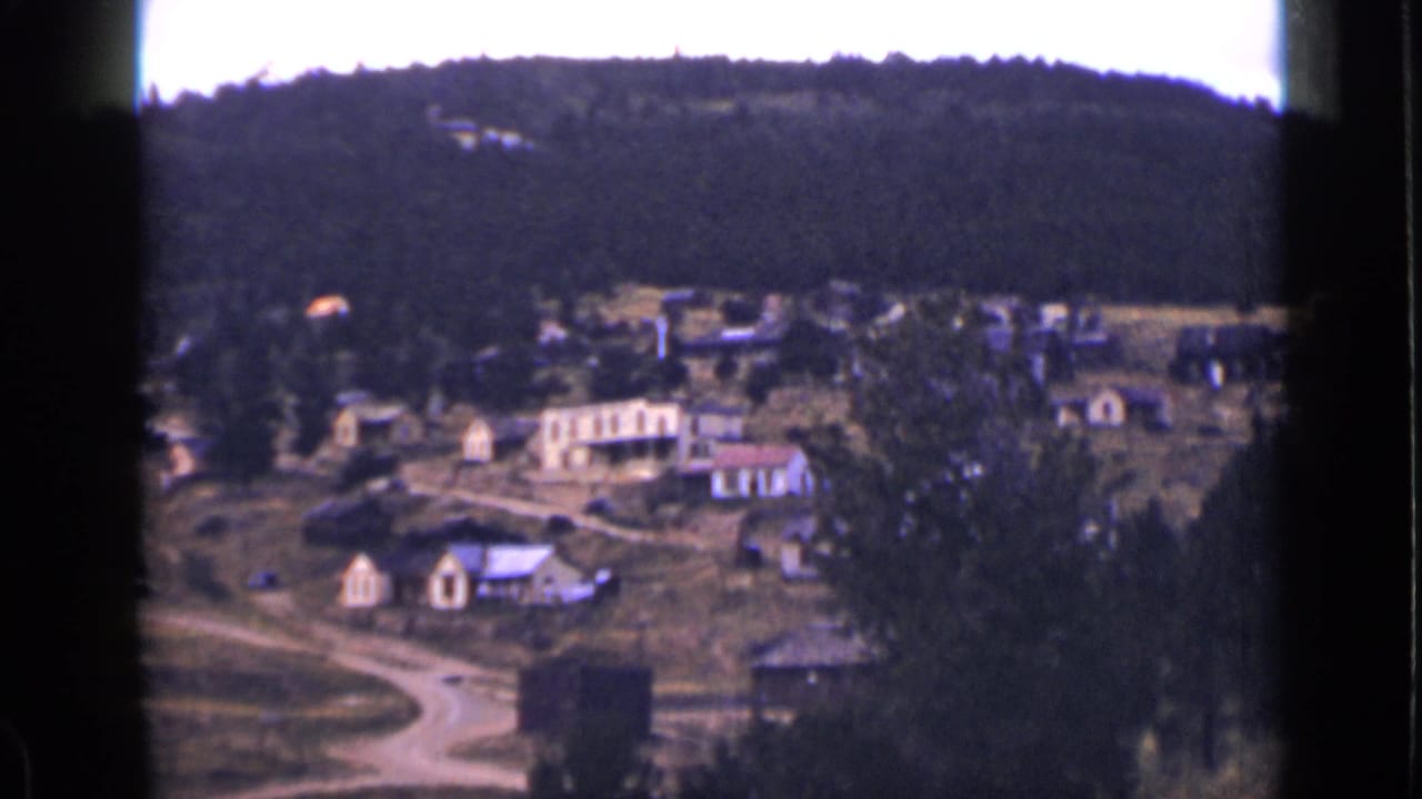 Small rural village seen from above with forested hills in the background.
