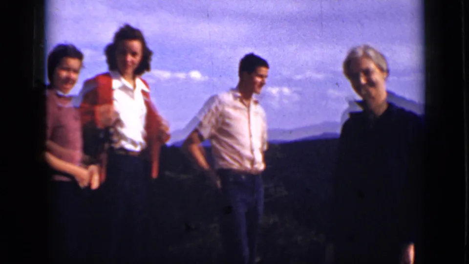 Four adults in 1939 Colorado travel footage pose at a mountain overlook, framed by dark slopes, pale sky, and soft 8mm color.