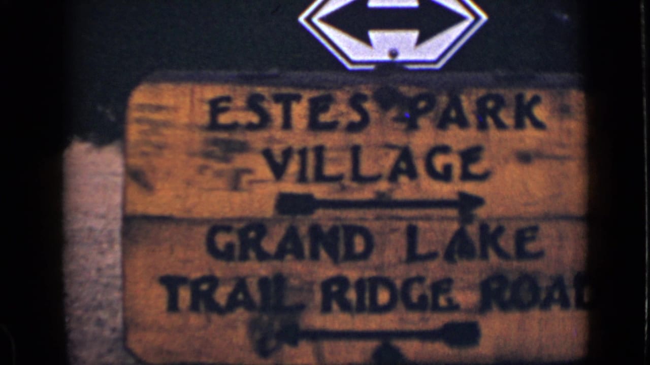 Weathered wooden sign with painted directions to Estes Park Village and Grand Lake Trail Ridge Road.