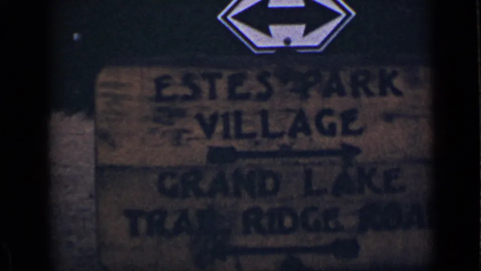 Darker 8mm frame of the Colorado road sign, with Estes Park Village and Grand Lake Trail Ridge Road lettering still discernible.