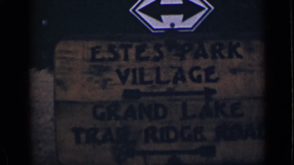 1939 Colorado 8mm frame showing a weathered roadside sign for Estes Park Village, Grand Lake, and Trail Ridge Road.
