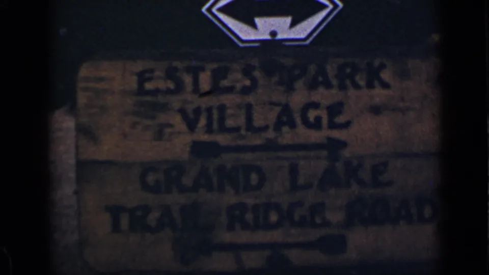 1939 Colorado home-movie frame with a soft, dark view of the Estes Park Village and Trail Ridge Road direction sign.