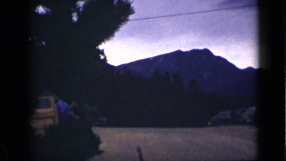 1939 Colorado 8mm frame showing a silhouetted mountain ridge, roadside trees, a vehicle, and a distant person in the foreground.