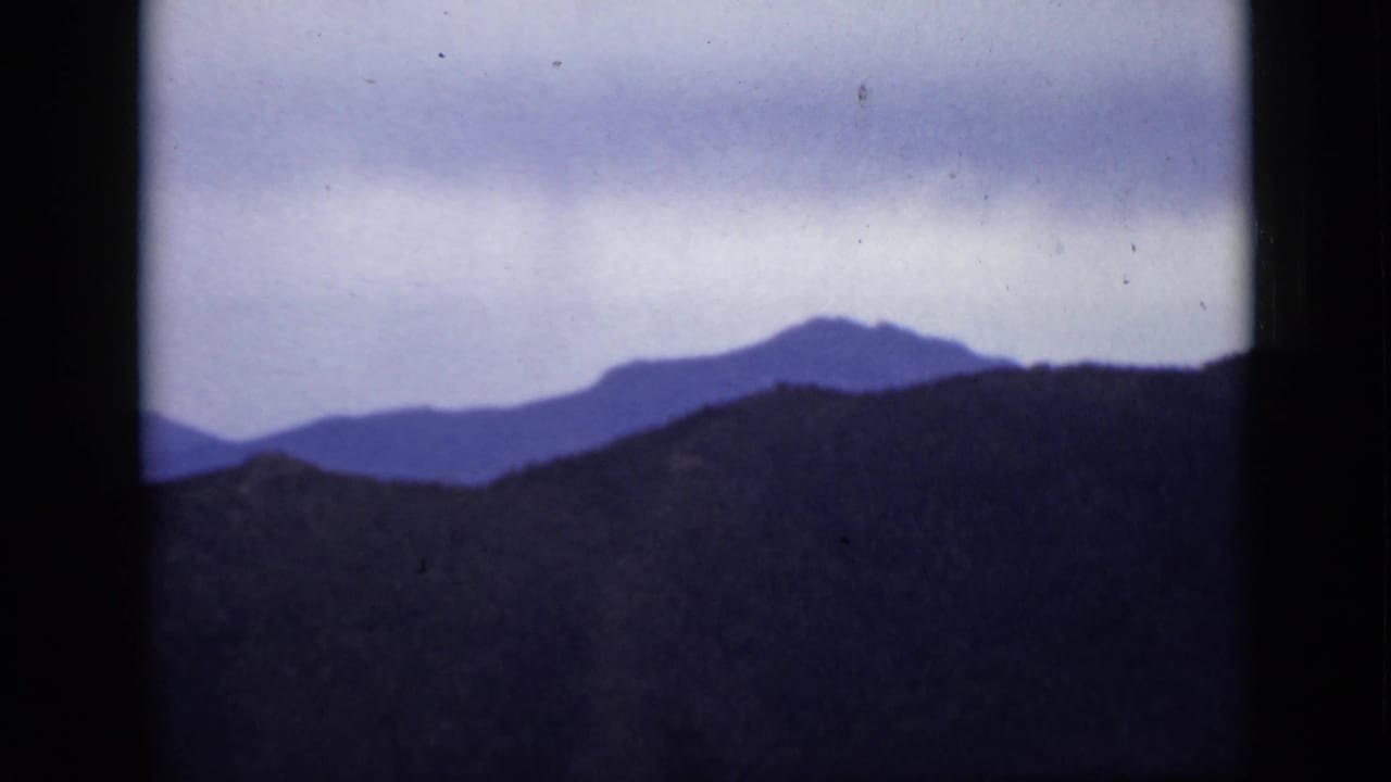 Dark mountain ridge beneath a cloudy pale sky with distant blue peaks.