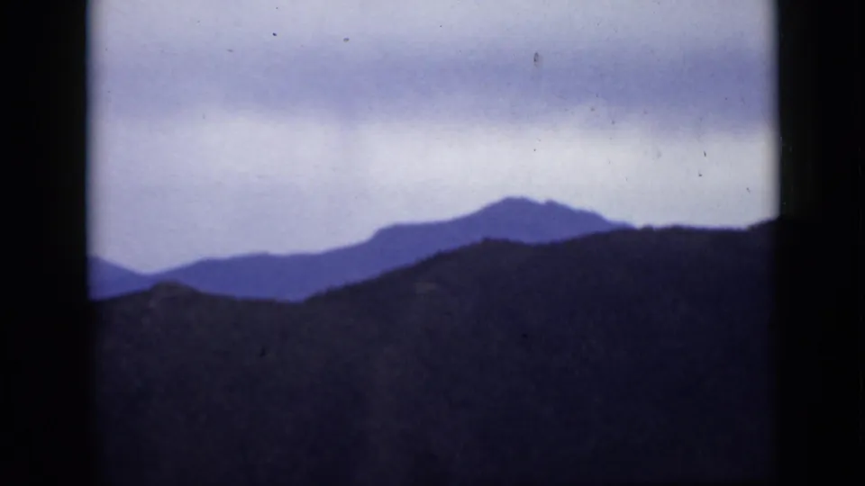 1939 Colorado 8mm frame showing layered mountain silhouettes under a cloudy sky, with soft grain and dark frame edges.
