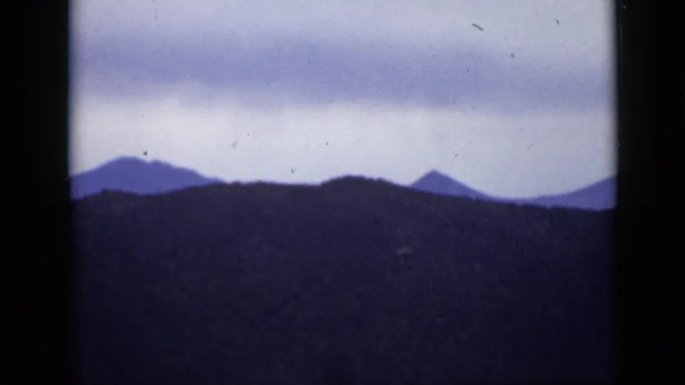 A Colorado mountain skyline is seen in a 1939 8mm frame, with dark ridges, soft focus, and a cloudy pale sky.