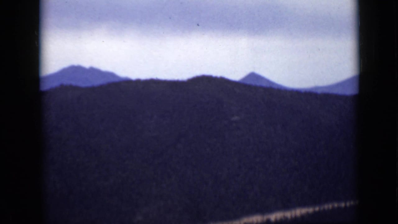 Dark forested mountain ridges under a pale sky with black film-frame edges.