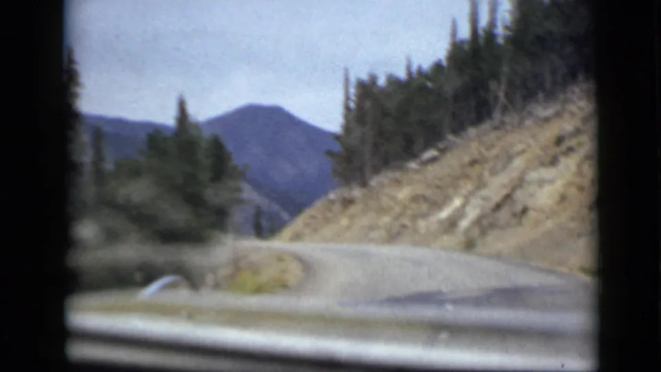 1939 Colorado 8mm road view from a moving vehicle, looking along a winding mountain road bordered by pines and rocky slope.