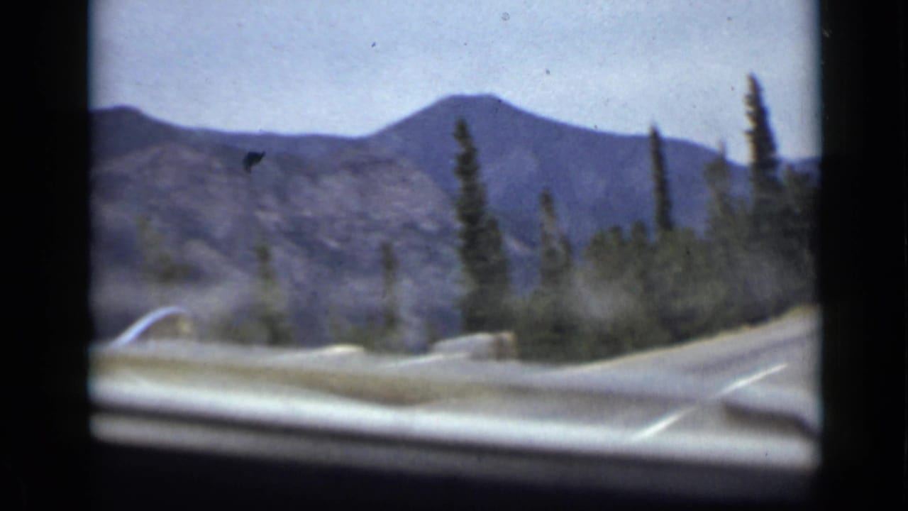 Curving mountain road with evergreens and distant ridges beyond the windshield.