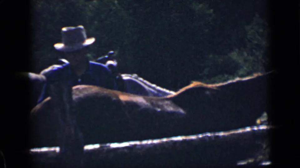 A man in a light-colored hat and dark shirt appears with a horse in 1939 Colorado riding footage, with another rider close by.