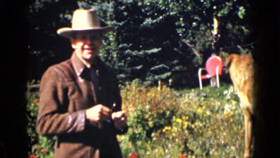 A man in a cowboy hat faces the camera in a 1939 Colorado garden while the red dog remains at the edge of the frame.