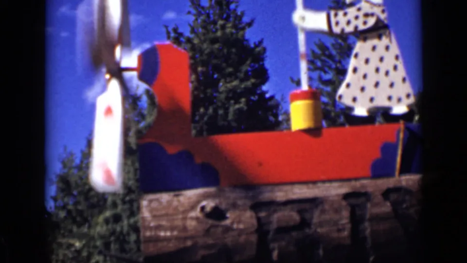 1939 Colorado 8mm frame of the folk-art windmill, with the churning figure partly visible above a red panel and evergreen backdrop.