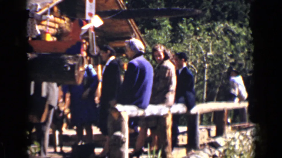Adults at a Colorado ranch stand beside fencing and a log structure, with trees behind them.