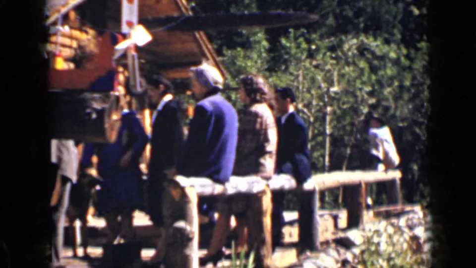 Colorado ranch visitors stand beside a wooden fence while a person moves near the edge of the frame.