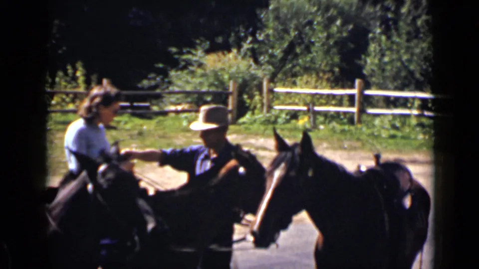 On a Colorado ranch, a mounted man appears to guide or hand something to a woman seated on a horse.