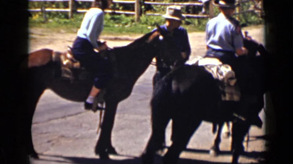 1939 Colorado home-movie still showing several riders on saddled horses gathered closely on a paved path near grass and fencing.