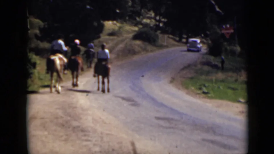 Colorado 1939 home-movie frame of riders on horseback on a dirt roadside, with a rounded automobile visible on the curving road.