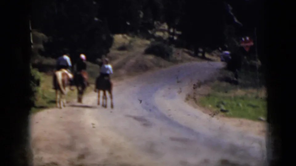 Colorado 1939 frame with horseback riders receding along a sunlit rural road, framed by trees and visible 8mm film edges.