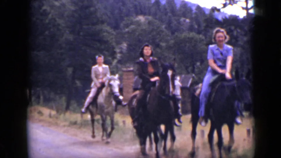 Three riders on horses pass near the camera in a wooded Colorado road scene from 1939 home-movie footage.