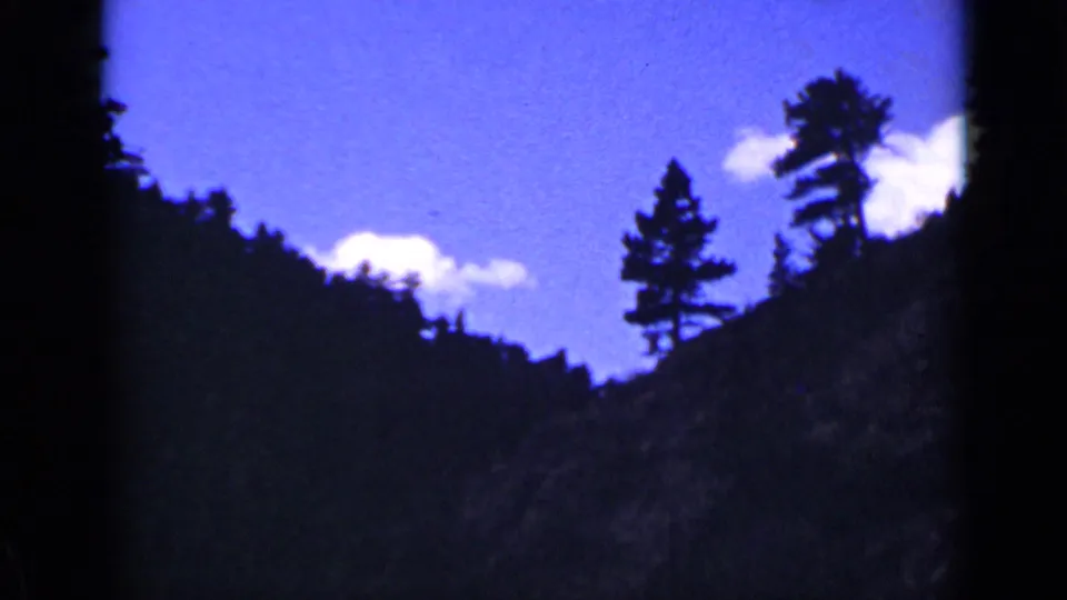Scenic 1939 Colorado home-movie view of pine trees and wooded hills silhouetted against blue sky and clouds.