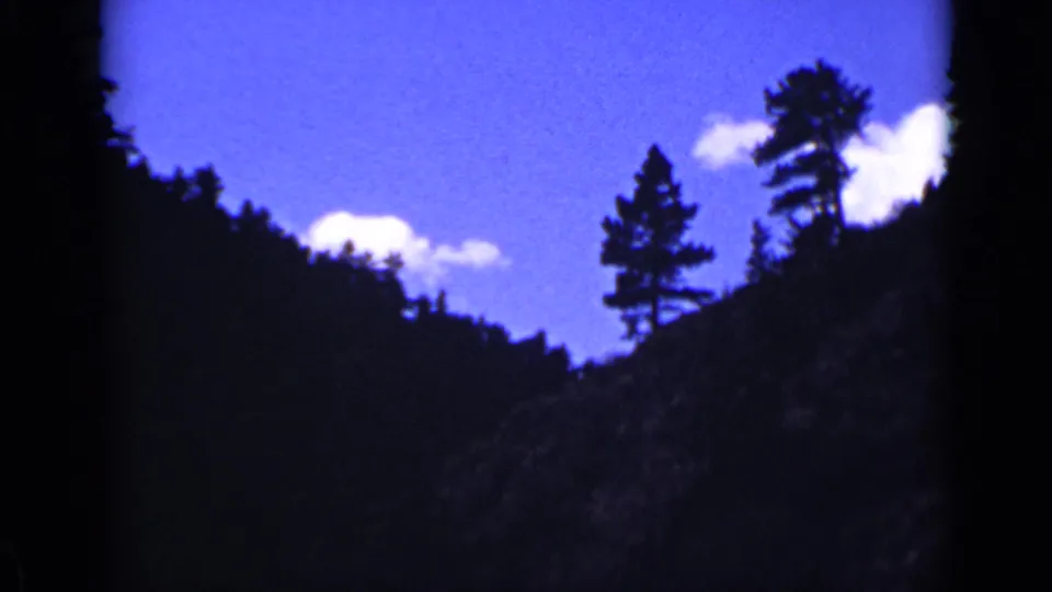 Colorado mountain landscape on 8mm film, with trees along the ridge and small clouds in a bright blue sky.
