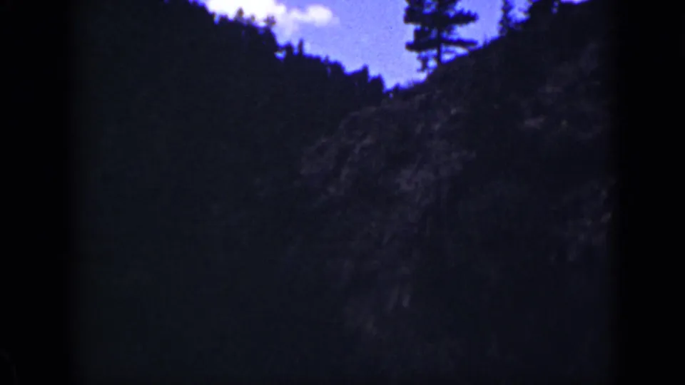 Final 1939 Colorado frame with a darker mountainside foreground, tree silhouettes near the ridge, and blue sky with clouds above.