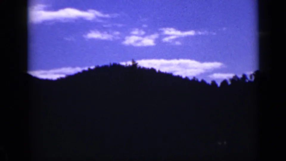 Colorado mountain ridge in silhouette beneath saturated blue sky and scattered white clouds on 8mm film.