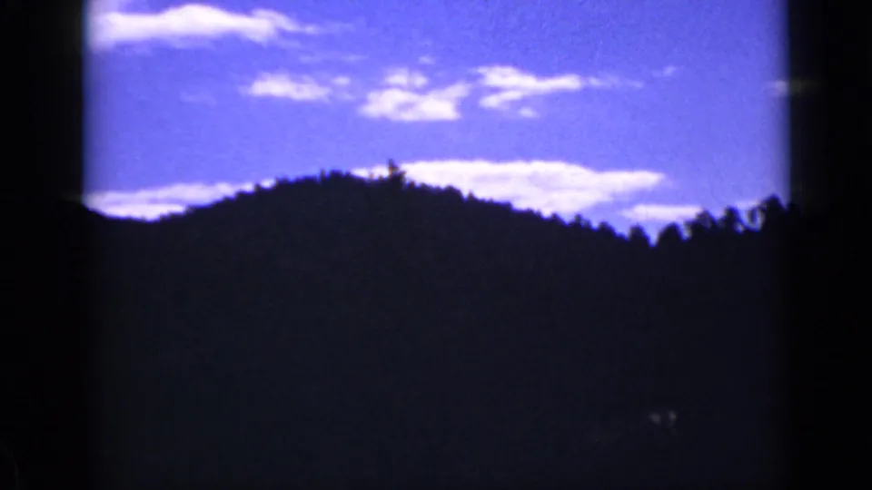 8mm frame of a Colorado forested ridge and treetops under a vivid blue sky with soft white clouds.