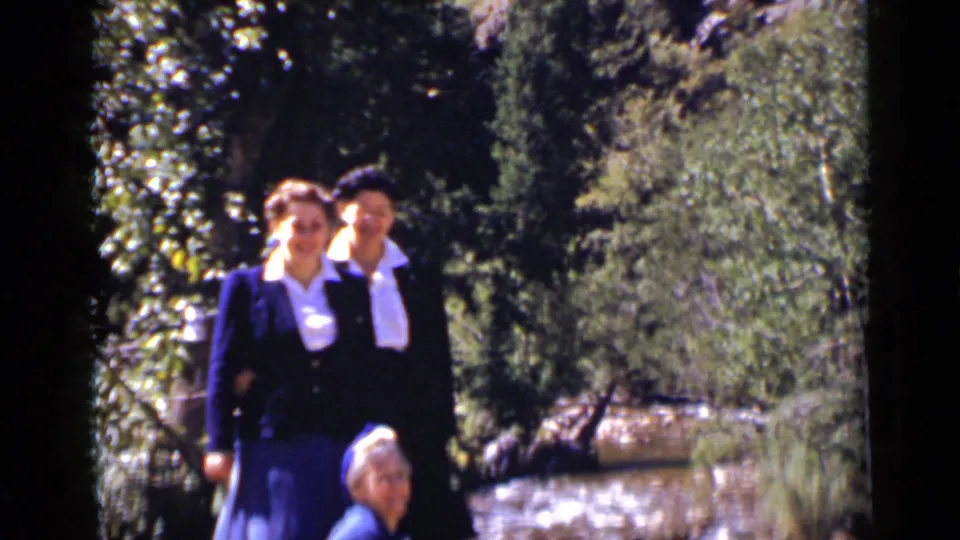 Two women stand behind a seated woman near a sun-dappled creek in Colorado, filmed on 8mm in 1939.