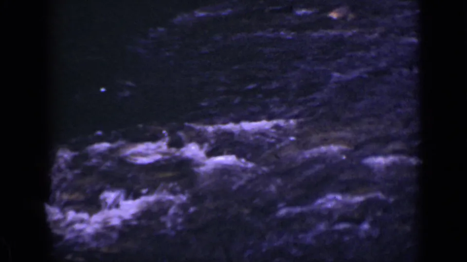 1939 Colorado 8mm frame showing dark stream water, rocks, and patches of white foam in the foreground.