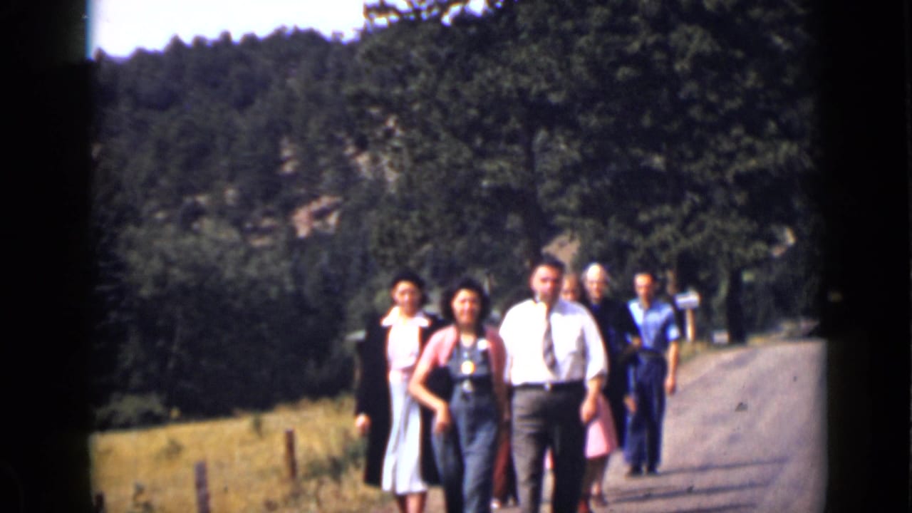 Adults in dress clothes walk toward the camera on a wooded unpaved road.