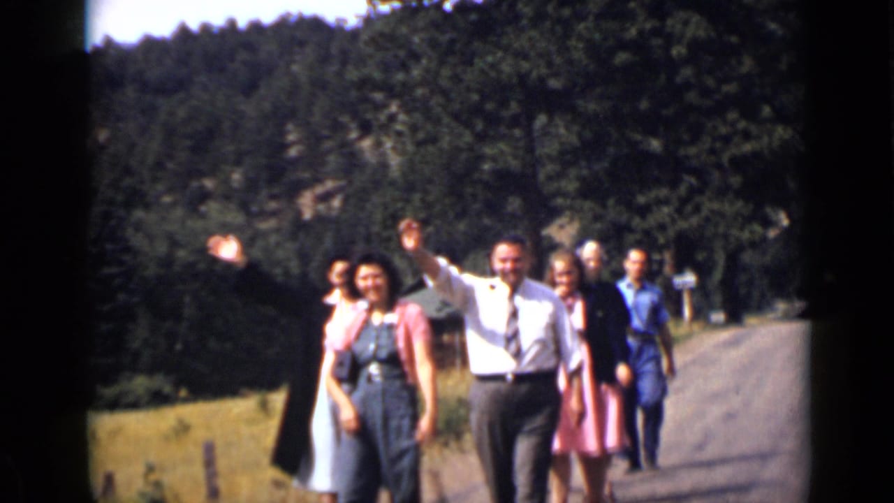 Adults walk closer on the road while one man raises his arm in a wave.